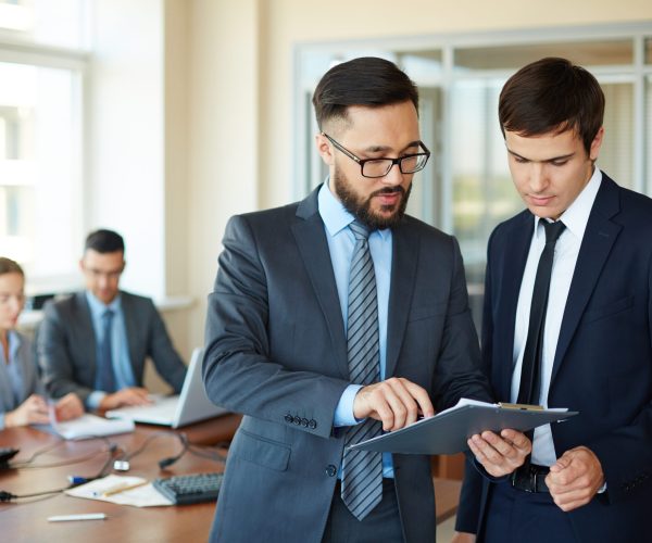 Paperwork Confident businessman pointing at document while explaining his idea to his partner on background of their colleagues